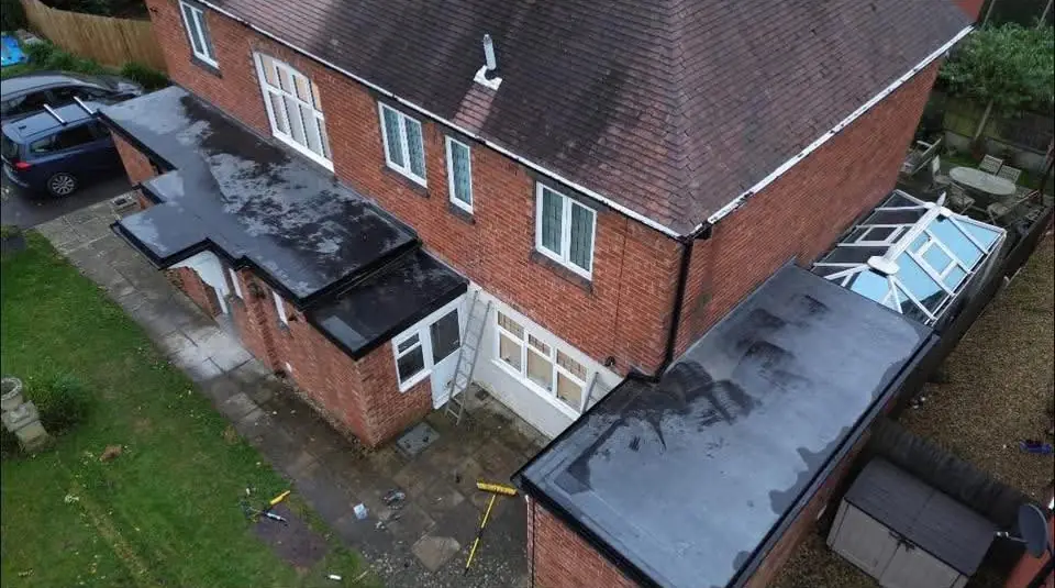 Drone view of a red-brick house in which the single-storey side and rear parts have new dark flat roofs